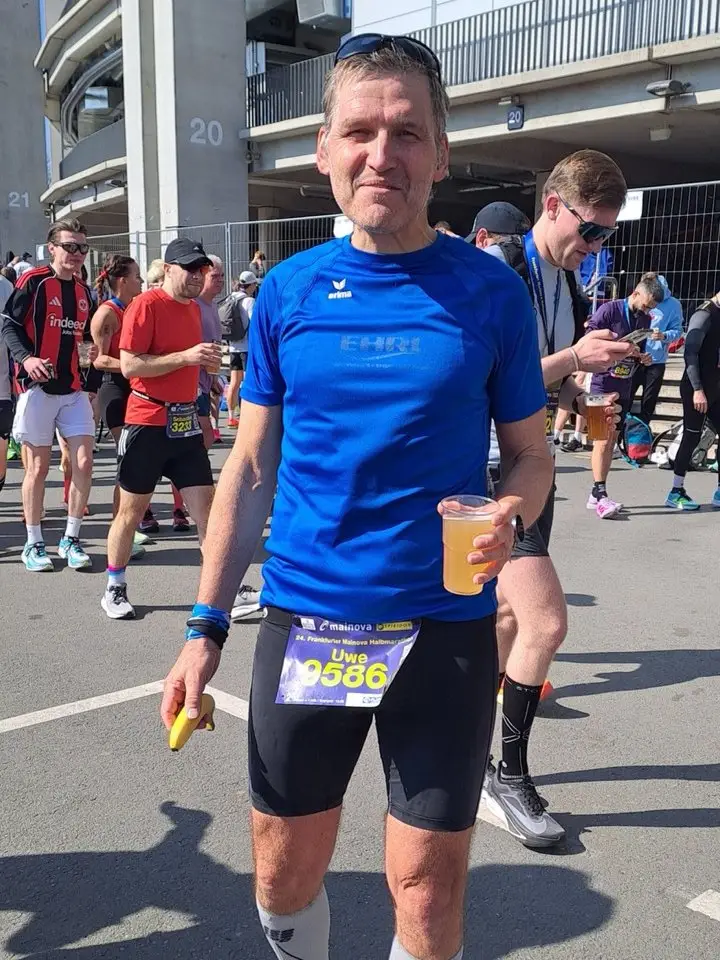 Uwe nach dem Frankfurter Halbmarathon mit Startnummer, Becher und Banane